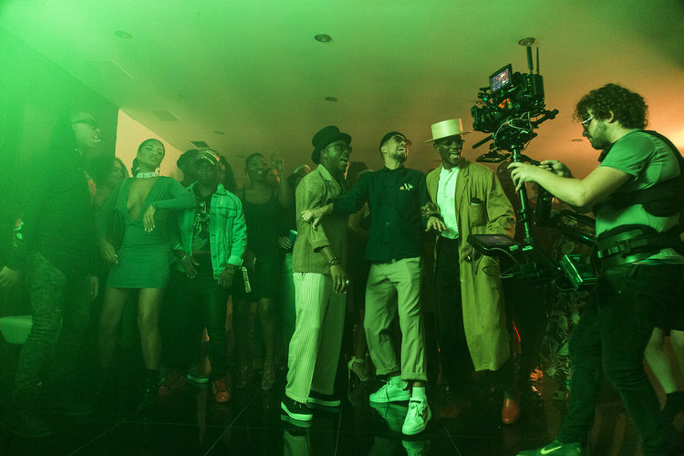 This photograph has a green tinge. It shows a group of man and women dancing for a film camera on the right of the image.
