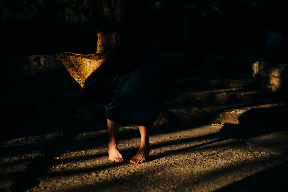 legs and feet of woman in pocket of sunshine with yellow dress blowing in wind