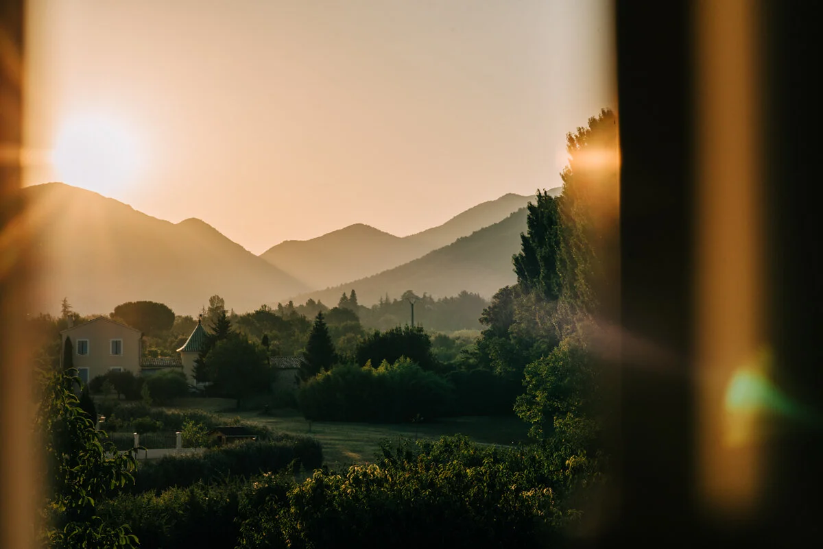 view through shutters of sun rising over rolling green hills