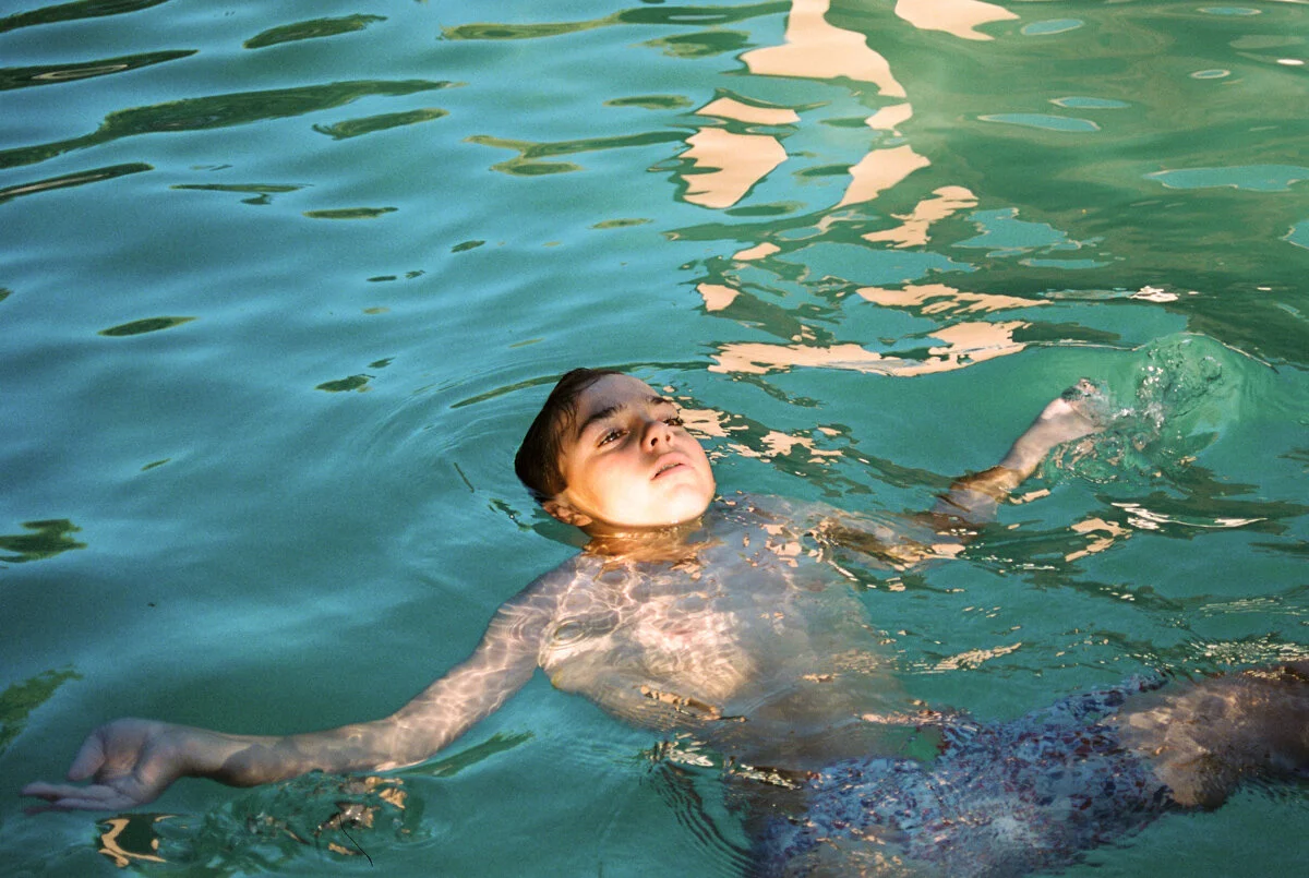 boy floating in green pool in late afternoon sun