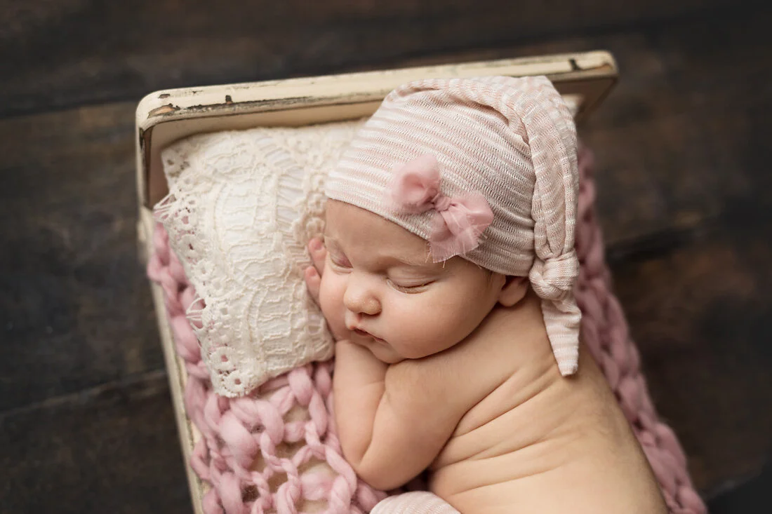 newborn girl in bed with pink bow hat