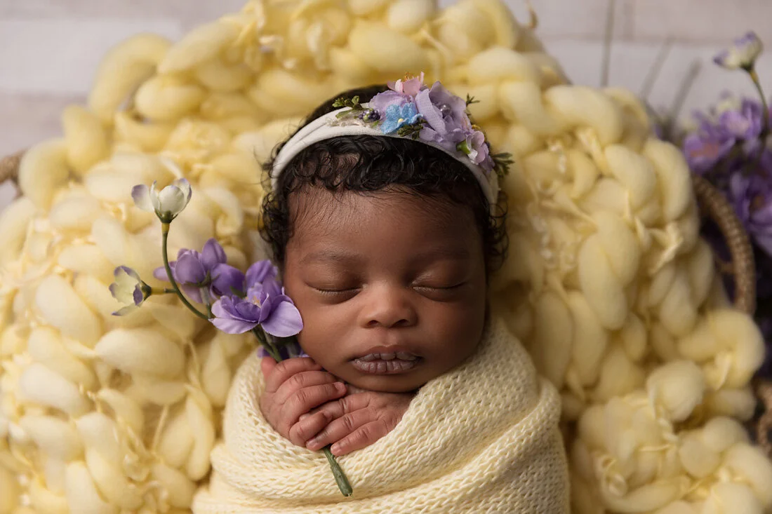 newborn girl holding purple flower on yellow