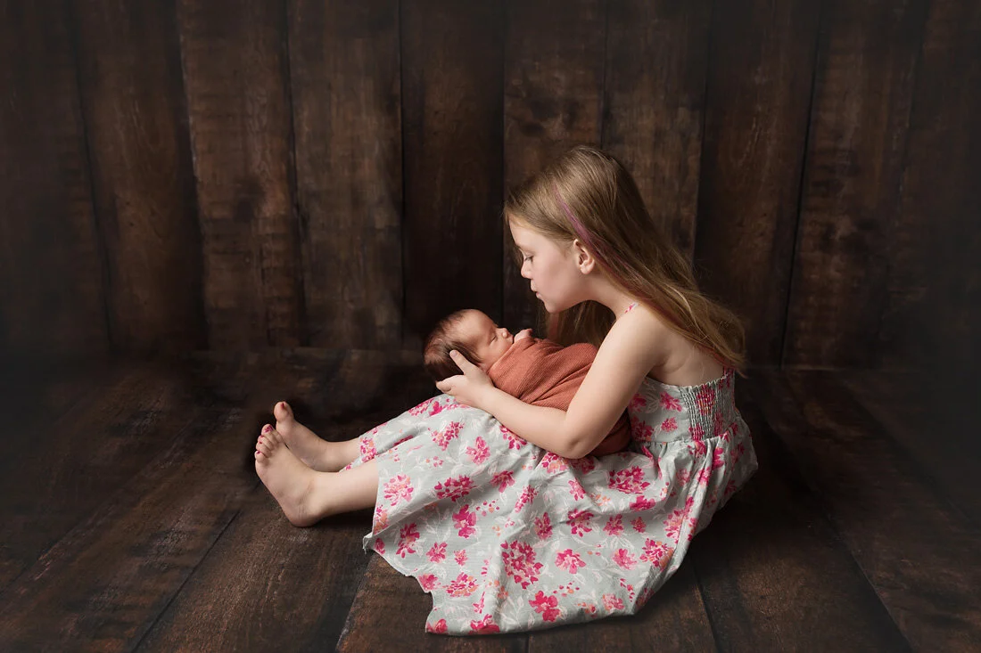 big sister holding newborn sister on her lap
