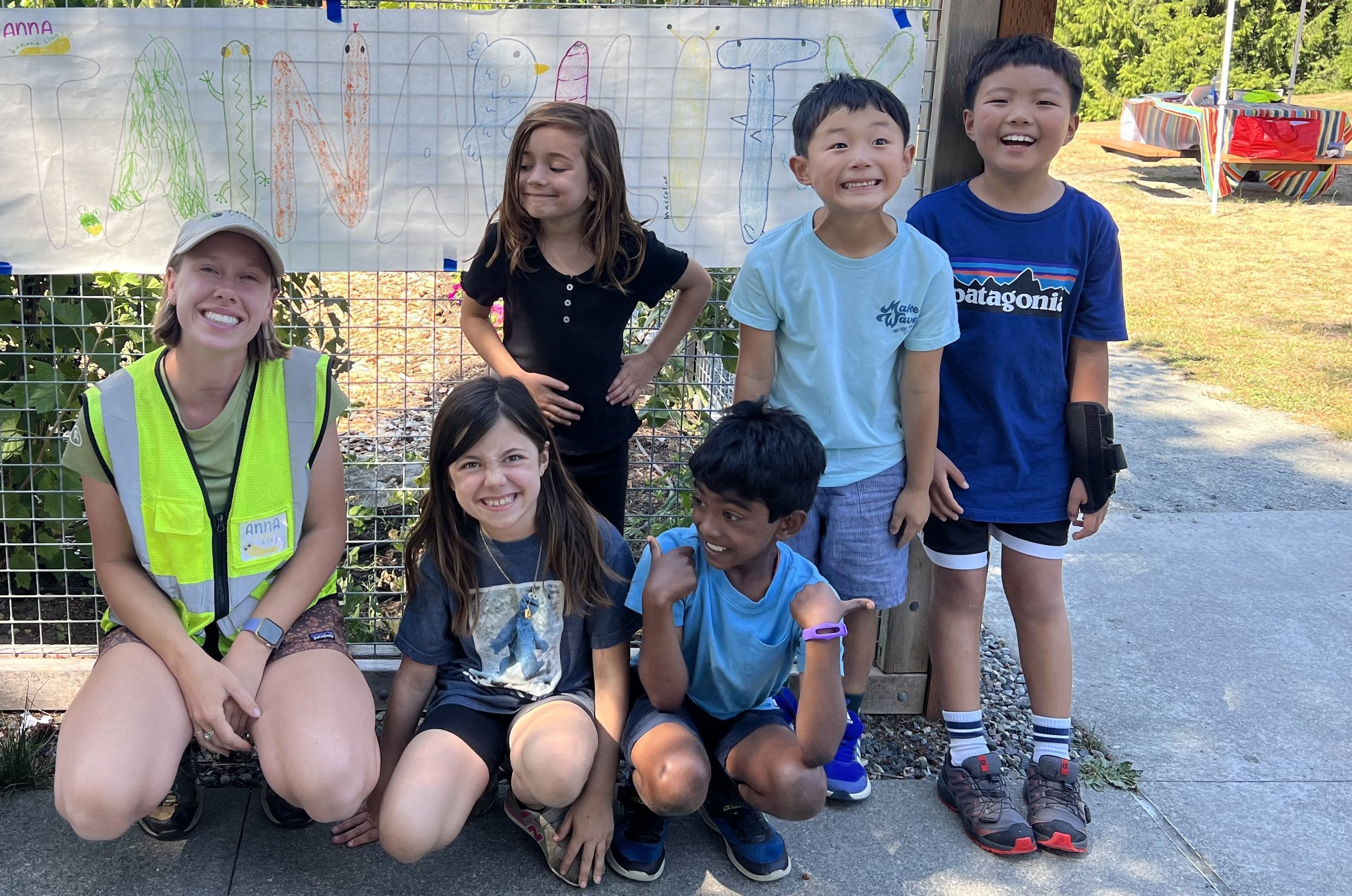 Five students and an educator smile in front of a hand-drawn camp sign