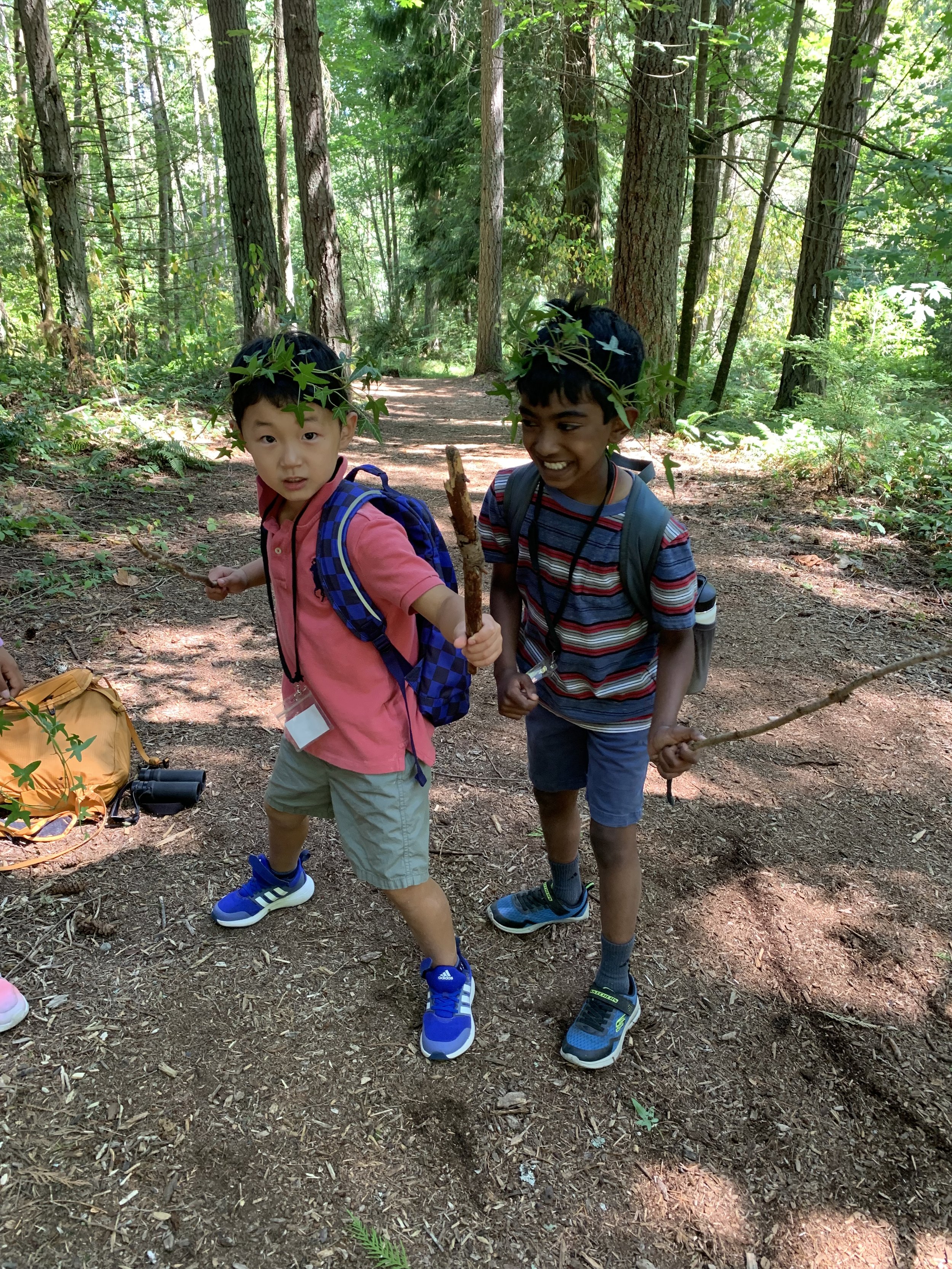 two students with sticks and ivy crowns pose in the forest
