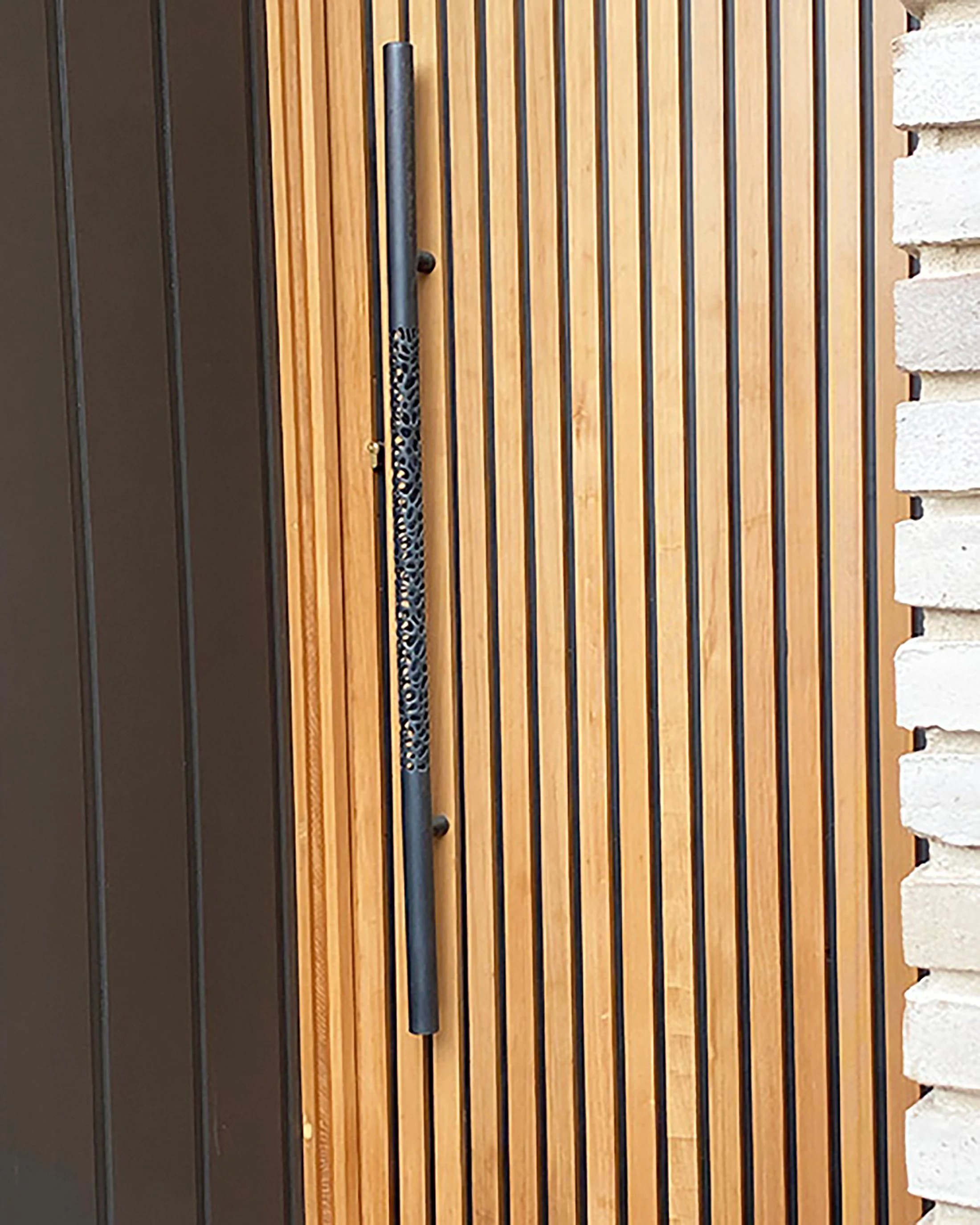 Large sculptural Morphic bronze entry door handle with dark patina installed on vertical cedar batten door.
