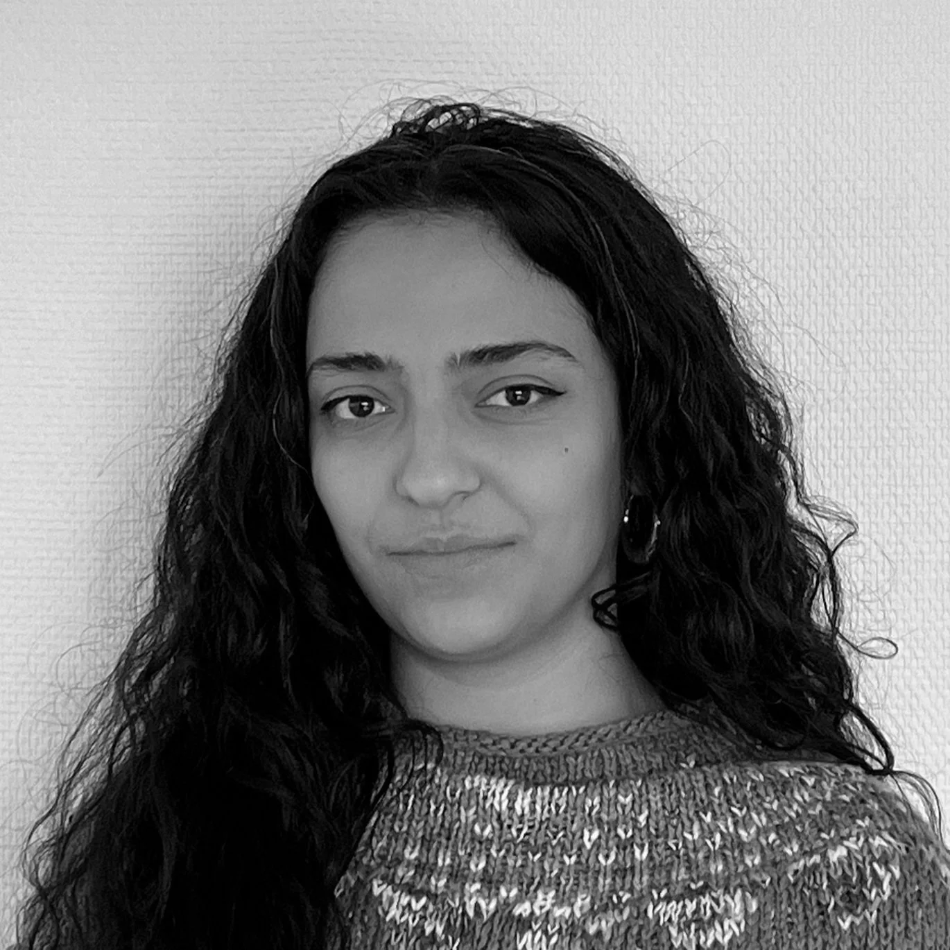 Portrait en noir et blanc d'une femme avec des cheveux bouclés foncés, portant un pull à motifs.