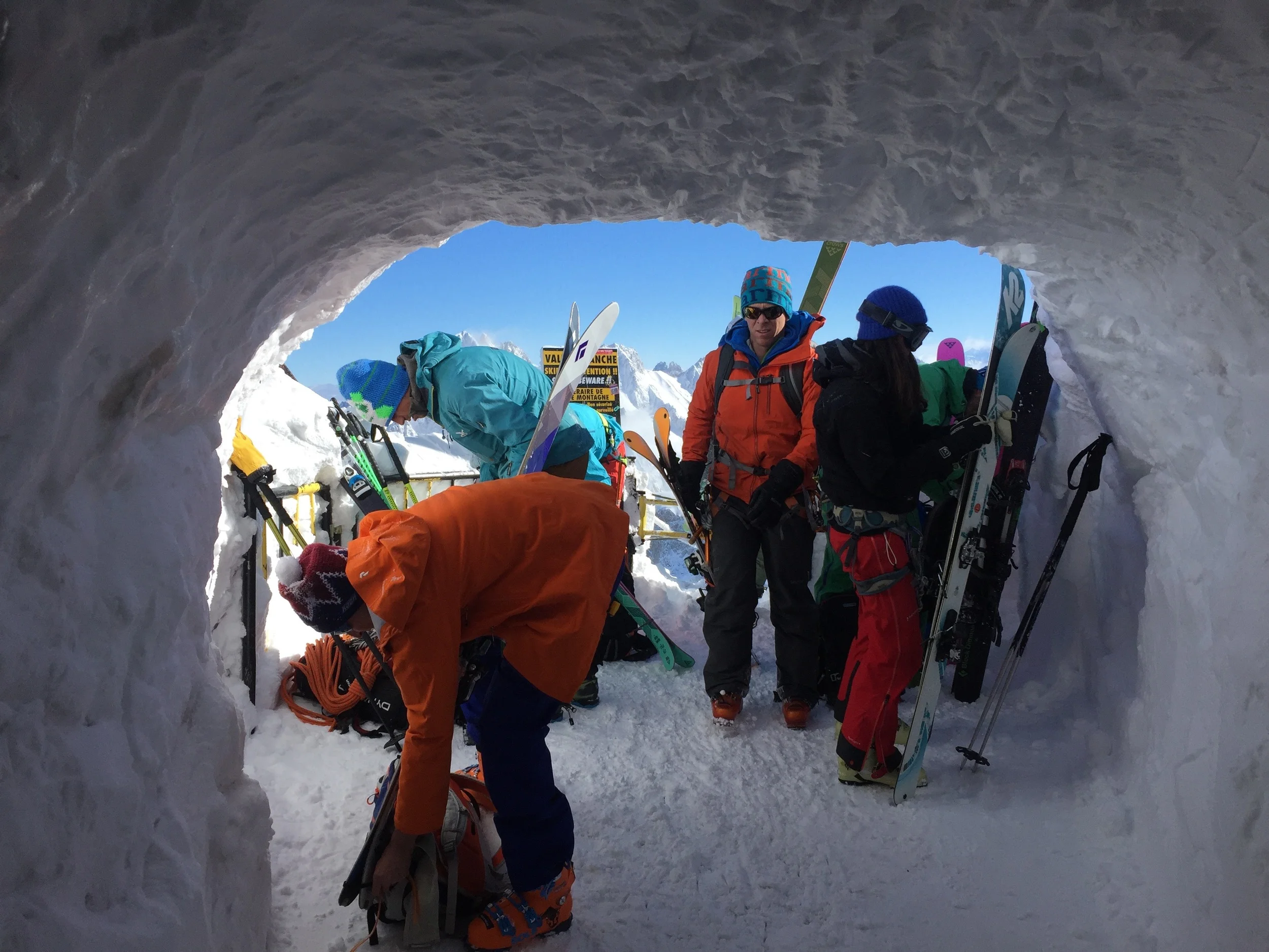 Skiers emerge from the ice tunnel and scramble to secure gear to their packs before making the trek on the arête