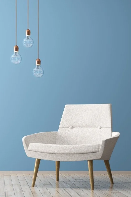 White mid-century modern armchair beneath three hanging pendant bulbs against a blue wall