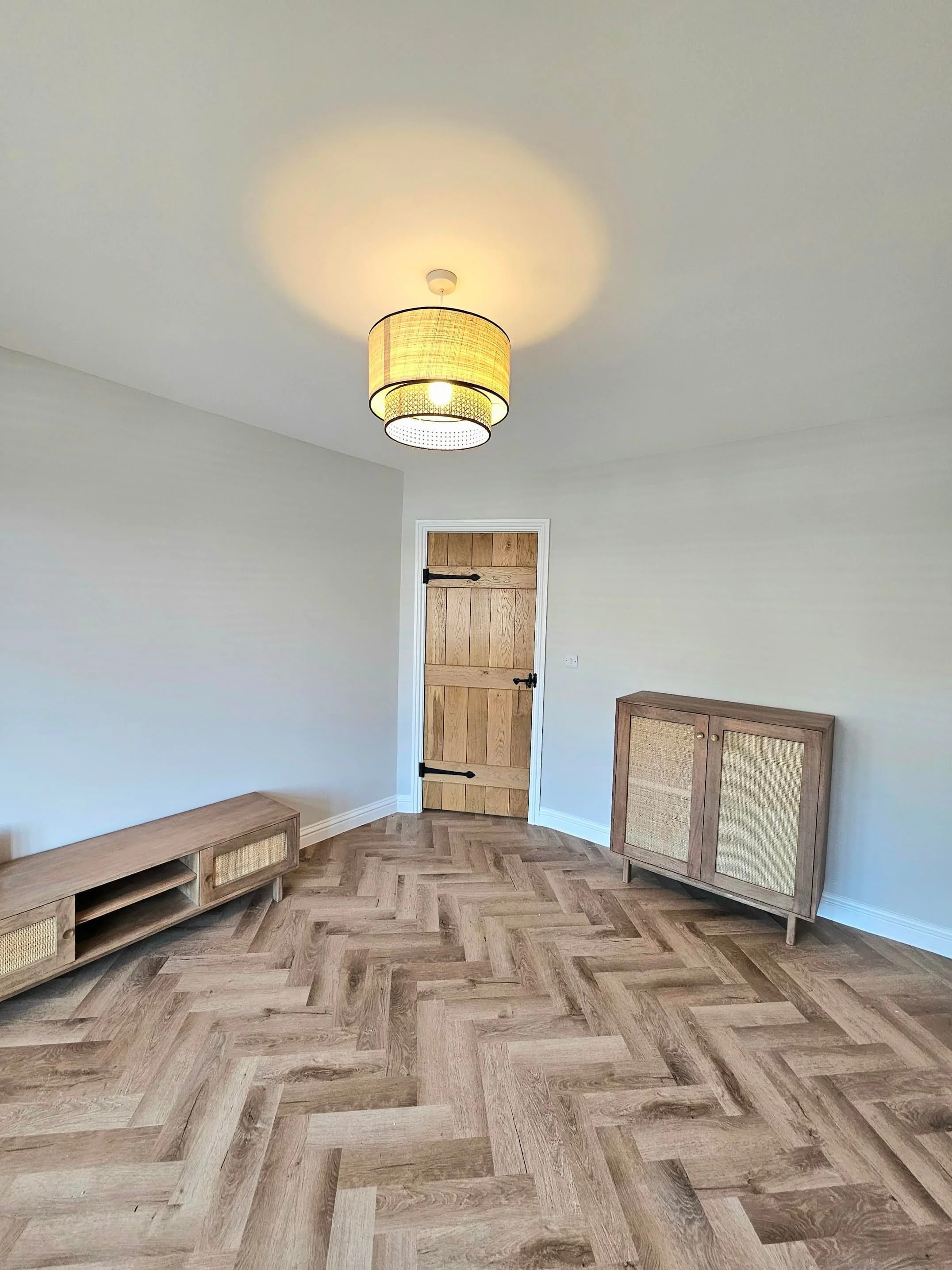 A corner of a room with a wooden door, two wooden cabinets with woven doors, and a ceiling light with a beige fabric lampshade.