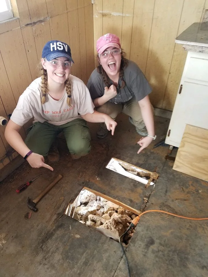 Megan Kucera and Sarah Jane from Team Hot Pants smiling after their hard work replacing rotting wooden floor.