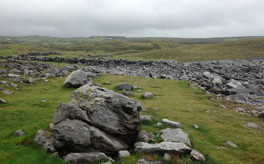 In The Burren, north of the Cliffs of Moher, Republic of Ireland, the rocky uplands provide plenty of material for building walls to keep grazing livestock confined. The stone walls appear to morph out of the earth and blend in with the naturally occurring erratics (large rocks) and other piles of stones.