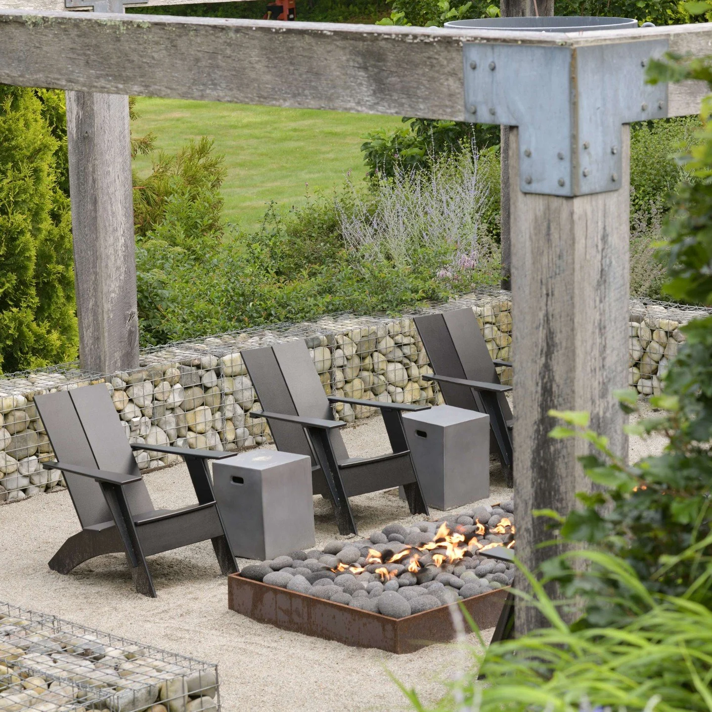 At The Studio in Rhode Island, gabion walls retain the sloped landscape around a linear fire feature, beneath an arbor of locally sourced and milled white oak.