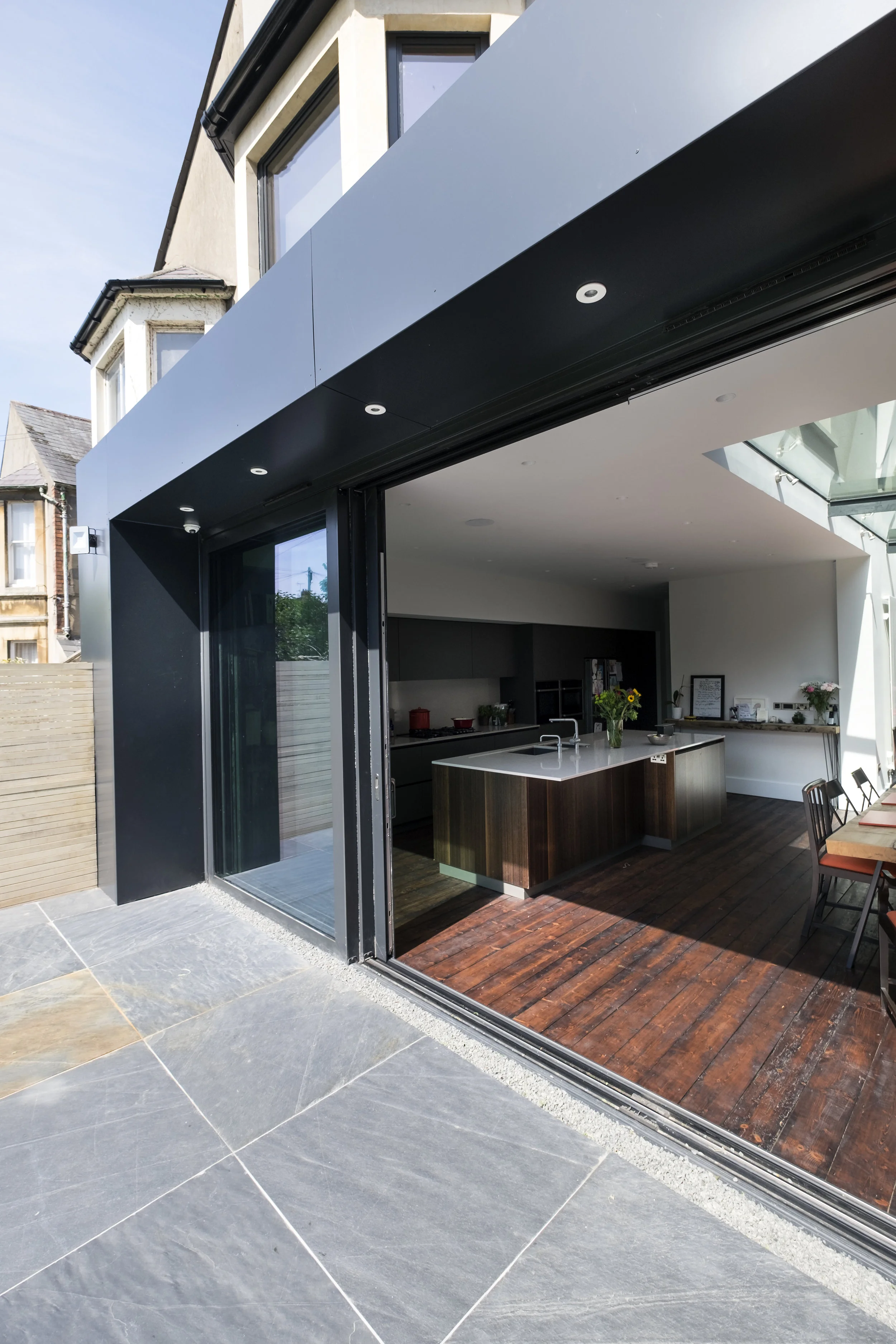 The dark grey Aluminium cladding, with full height lift and slide solar control glass doors, reclaimed stained timber floorboards and Welsh slate tiles, blend beautifully the outside with the inside ; the old and the new. The existing Victorian architectural charm is retained with colours and textures of its time, whilst the additions unashamedly reflect the way we build today. 