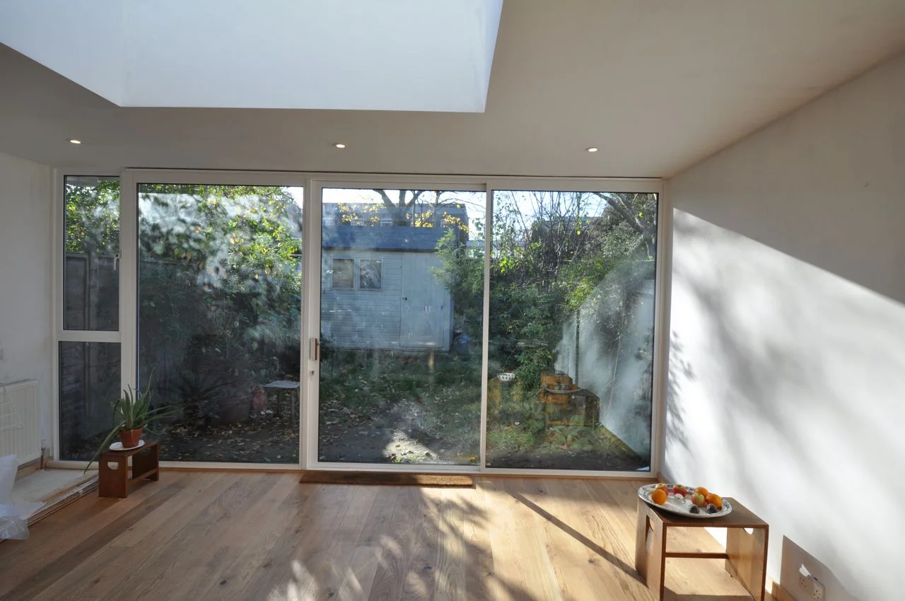 Anderton Close is a late 1960’s housing terrace, of basic construction and compressed internal spaces, with the original properties generally requiring much improvement works to bring up to current standards. The brief, from the professional artist owner-occupier, was for a new single-storey rear extension with extensive internal remodeling for an improved kitchen/ living space, new family bathroom and ground floor WC, new study room, refurbished bedrooms and hall spaces and general internal and external alterations and improvements. The aim was to supply this modest residential extension project, with a budget of only £69,500 (equating to approx. £650 per sq m) to as high a standard as possible, creating a calm, generous and light-filled dwelling. The rear extension was designed to the maximum volume achievable under permitted development rights. Much effort was taken in the structural design to recess all new steel columns and beams, so that the extension is continuous with the original room. The fully glazed rear facade and the rooflight were also installed with frames concealed by wall, floor and ceiling structure. Daylight floods into the space, changing its quality throughout the day. Bathroom and hall spaces were also opened up. Clerestory windows and new translucent glazing to the entrance door are echoed by the ‘light-beam’ of the recessed alcove shelf in the bathroom. © jake ireland architects 2007 - 2015