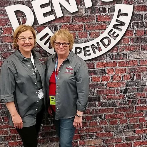 two people posing next to a discover denton logo on a fake brick wall