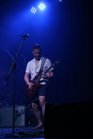 a picture of a person playing guitar on a stage under a bright light