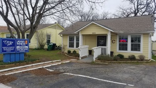 a picture of a yellow house in a parking lot with a blue business sign outside of the house near the end of the sidewalk.