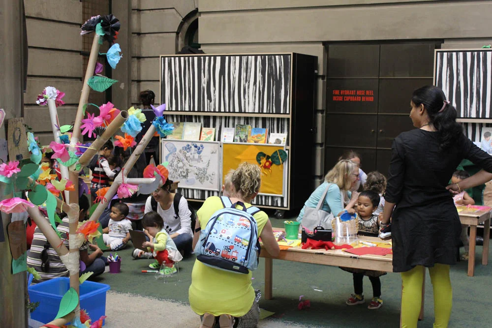 Participants' flowers and leaves fill the cardboard tree, 'Come play in our garden' in Play Pod, State Library Victoria.