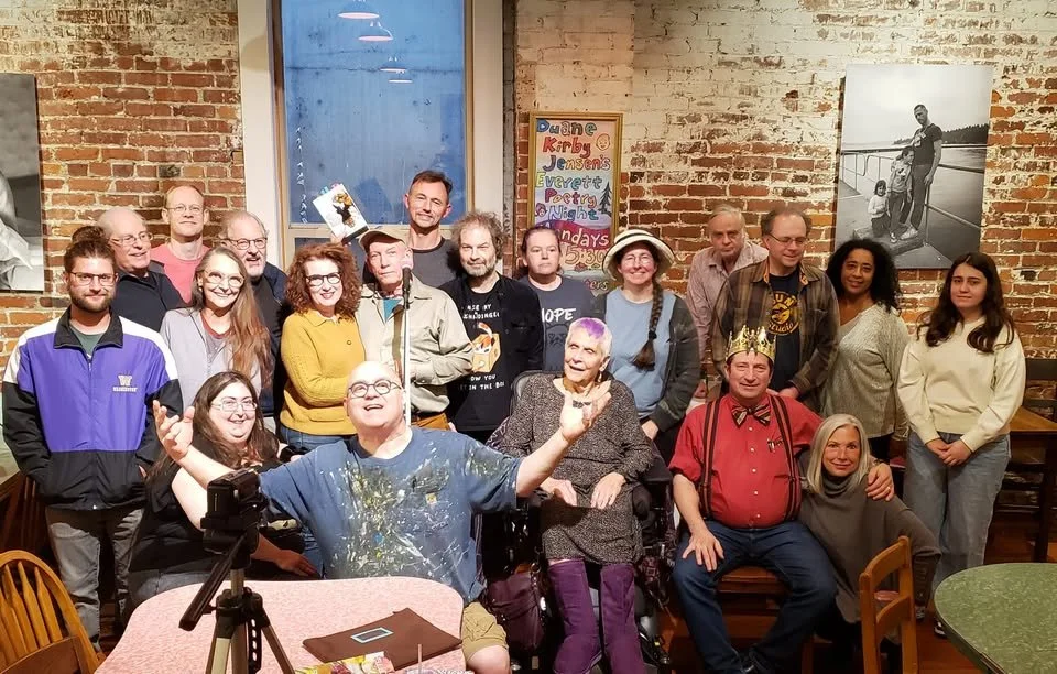 Group photo of the Everett Poetry Night community gathered in front of a brick wall at The Sisters Restaurant