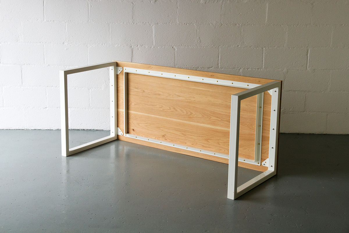 Cord Industries Nola table in oak with white legs, laid on side to show hardware details.