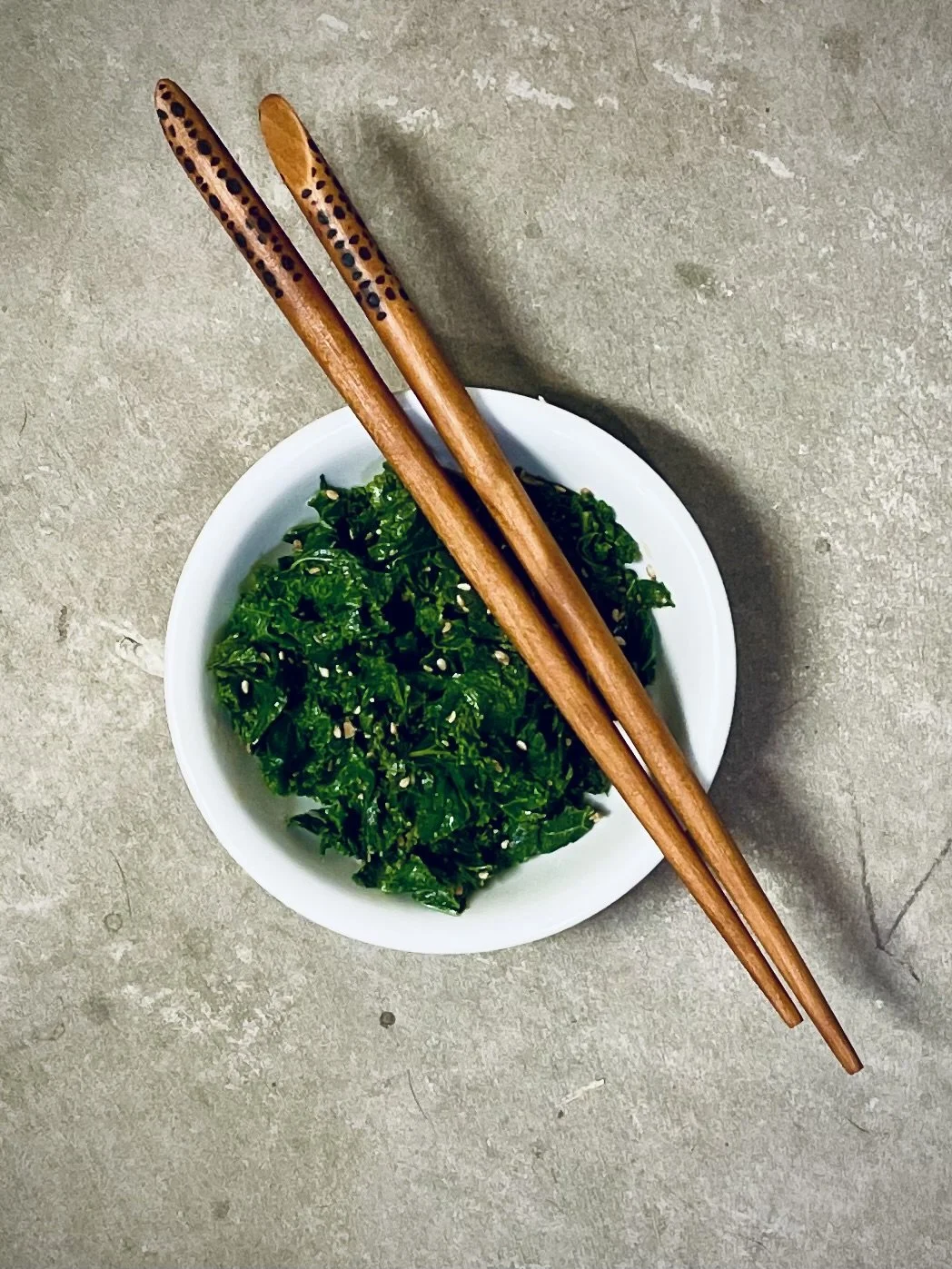 Handmade chopsticks sitting atop a bowl of seaweed salad.