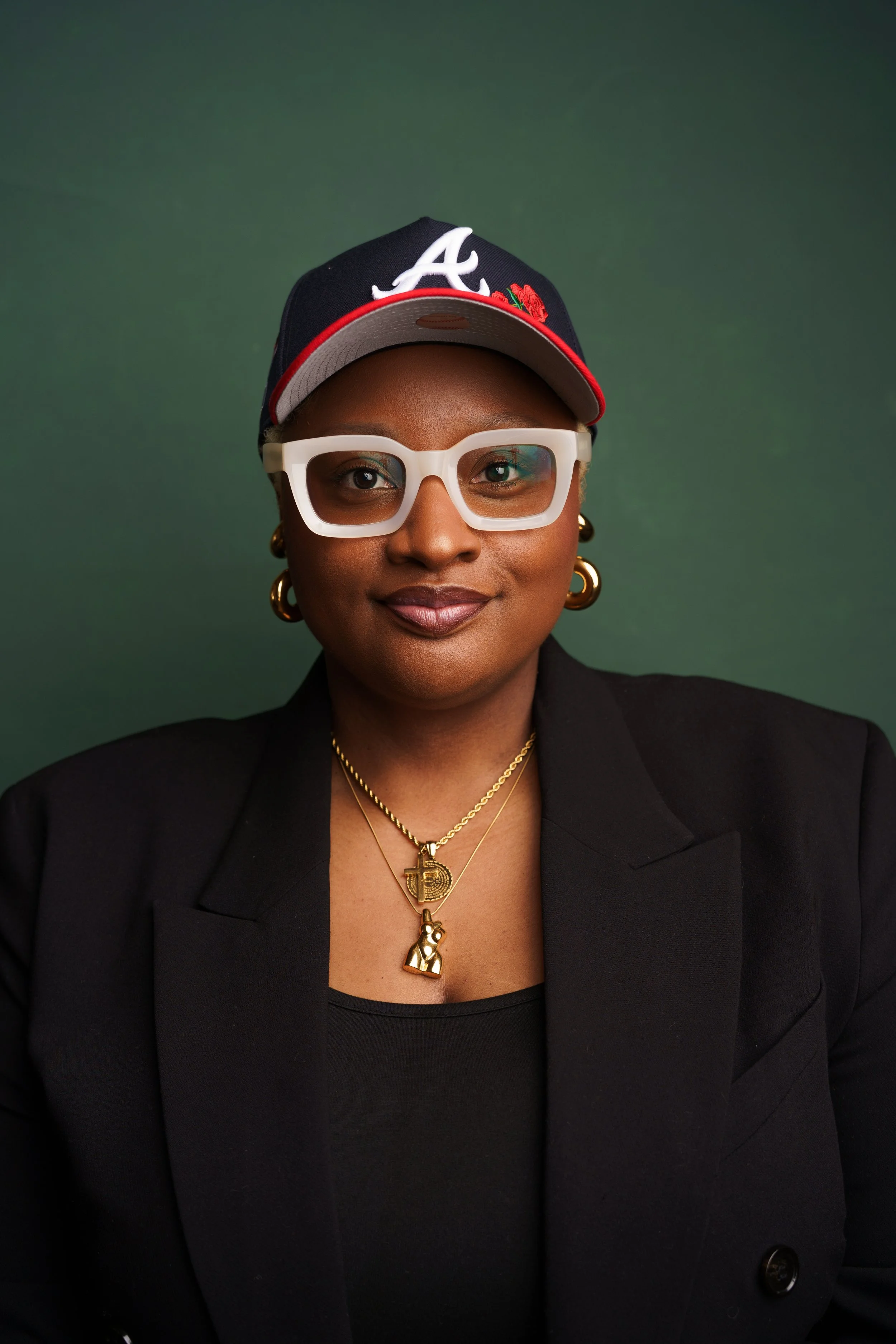 Beautiful Black woman in white glasses wears an Atlanta Braves hat on a green backdrop