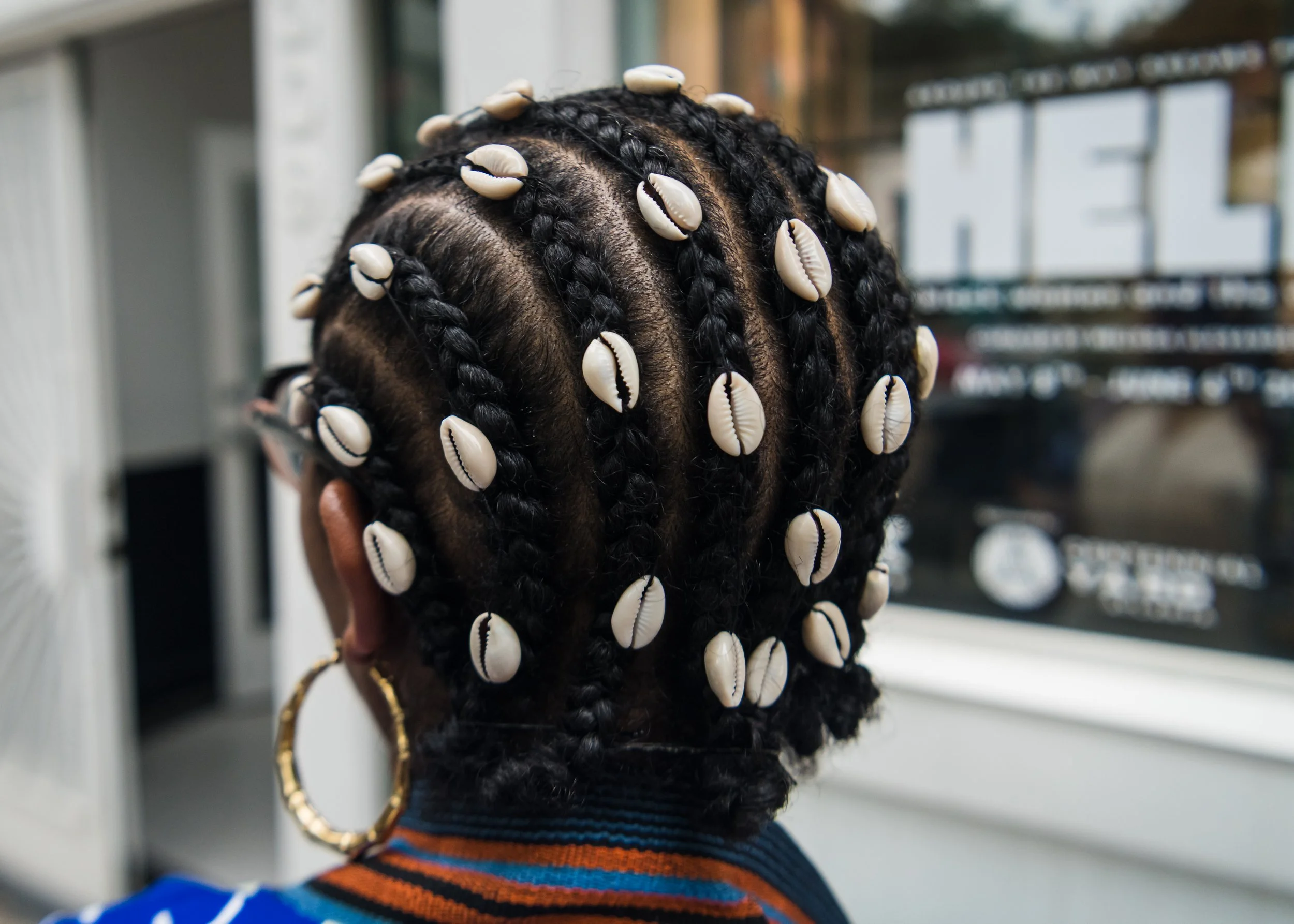 Black woman with cowrie shells in her crownrows stands in front of museum doors
