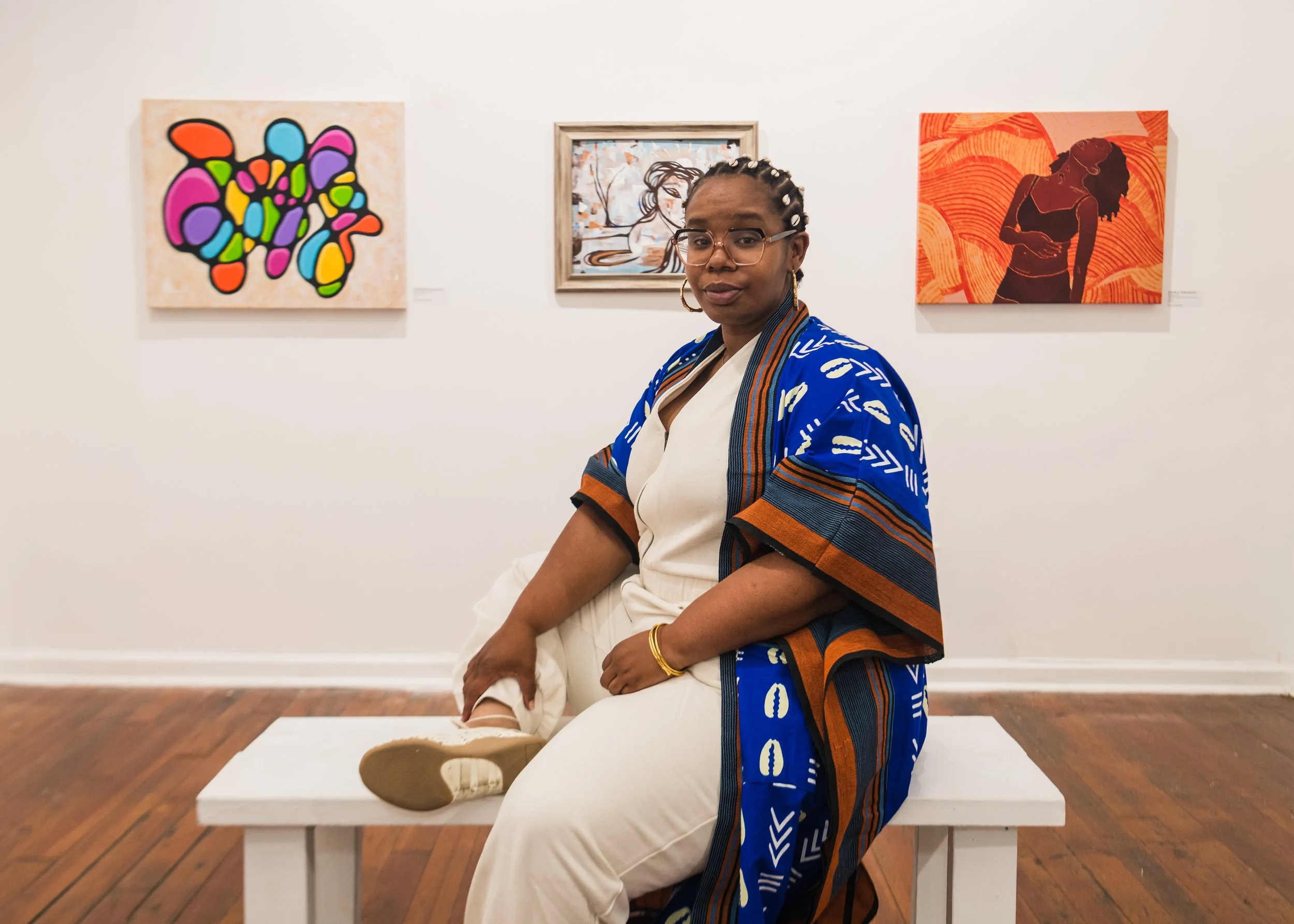 Black woman in a blue robe poses in front of womb health artwork in a gallery