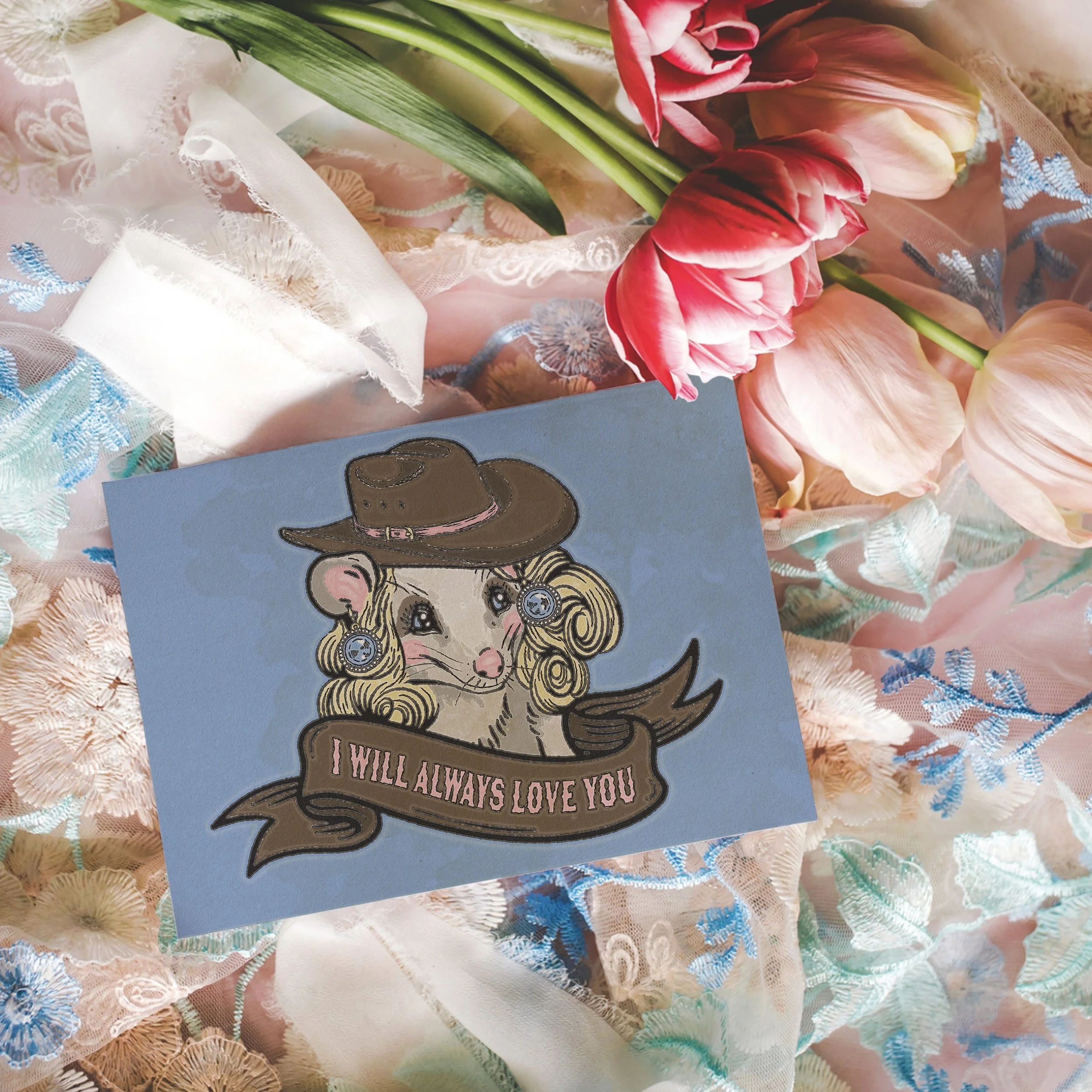 a card on top of a lacy floral background with pastel colors. The card is blue and features a possum with a blond wig and blue earrings. She has a ton of makeup on and a cowboy hat. A banner says "I will always love you."