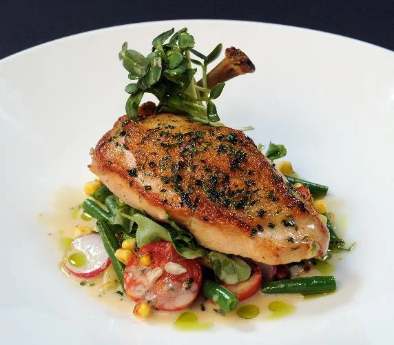 Chicken over a bed of vegetables including radish, green beans, mache, fresh corn/ sunchoke cream