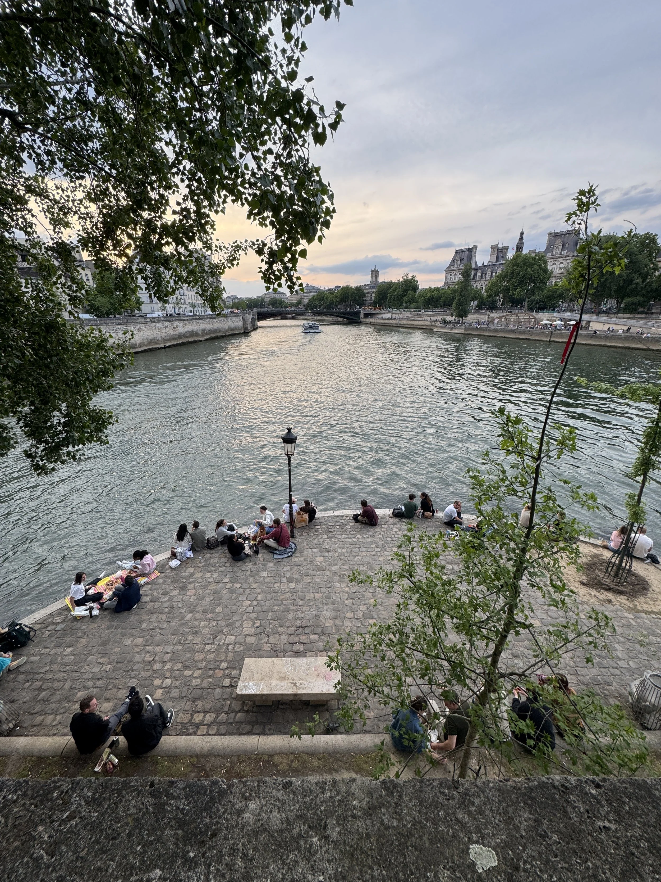 A wide view of the tip of the Île Saint Louis in Paris from above with people sitting along the banks below.