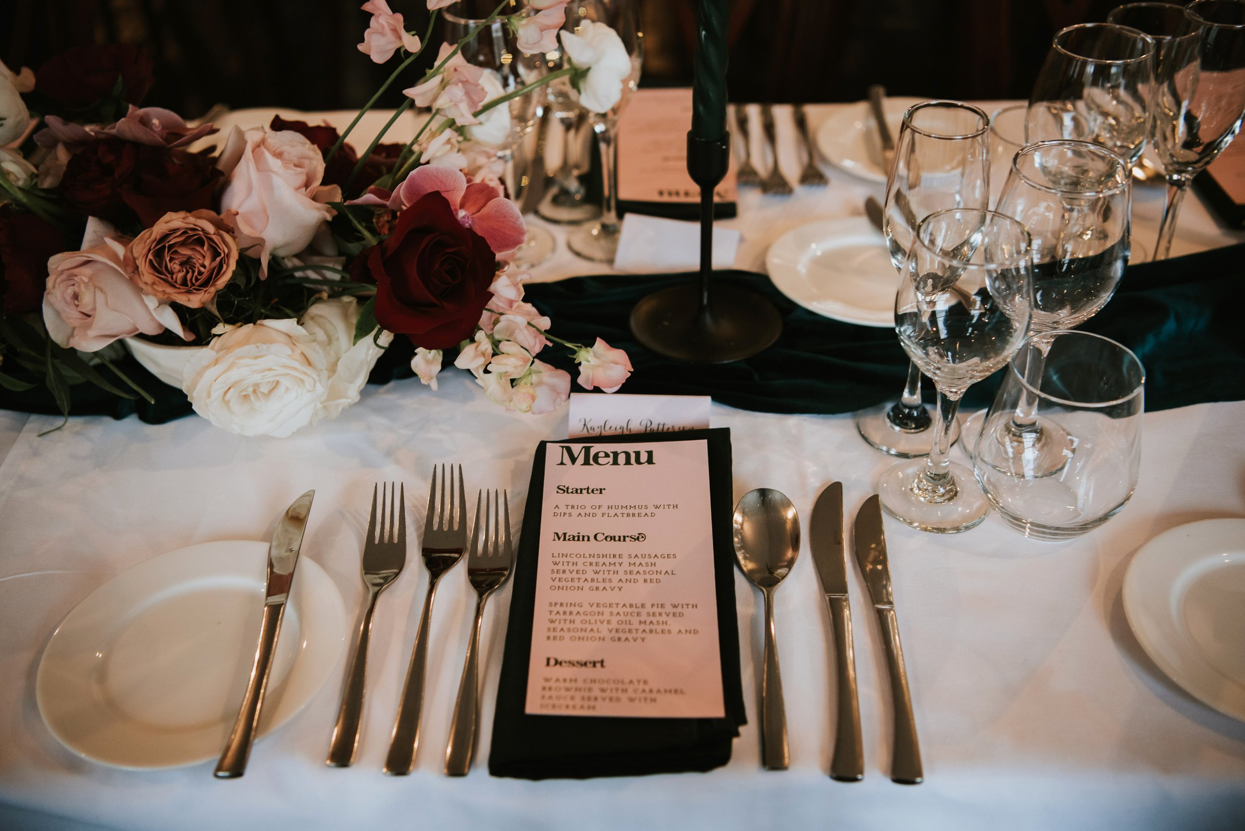 Elegant table setting with a floral centerpiece, wine glasses, a menu, and silverware arranged on a white tablecloth for a formal event.