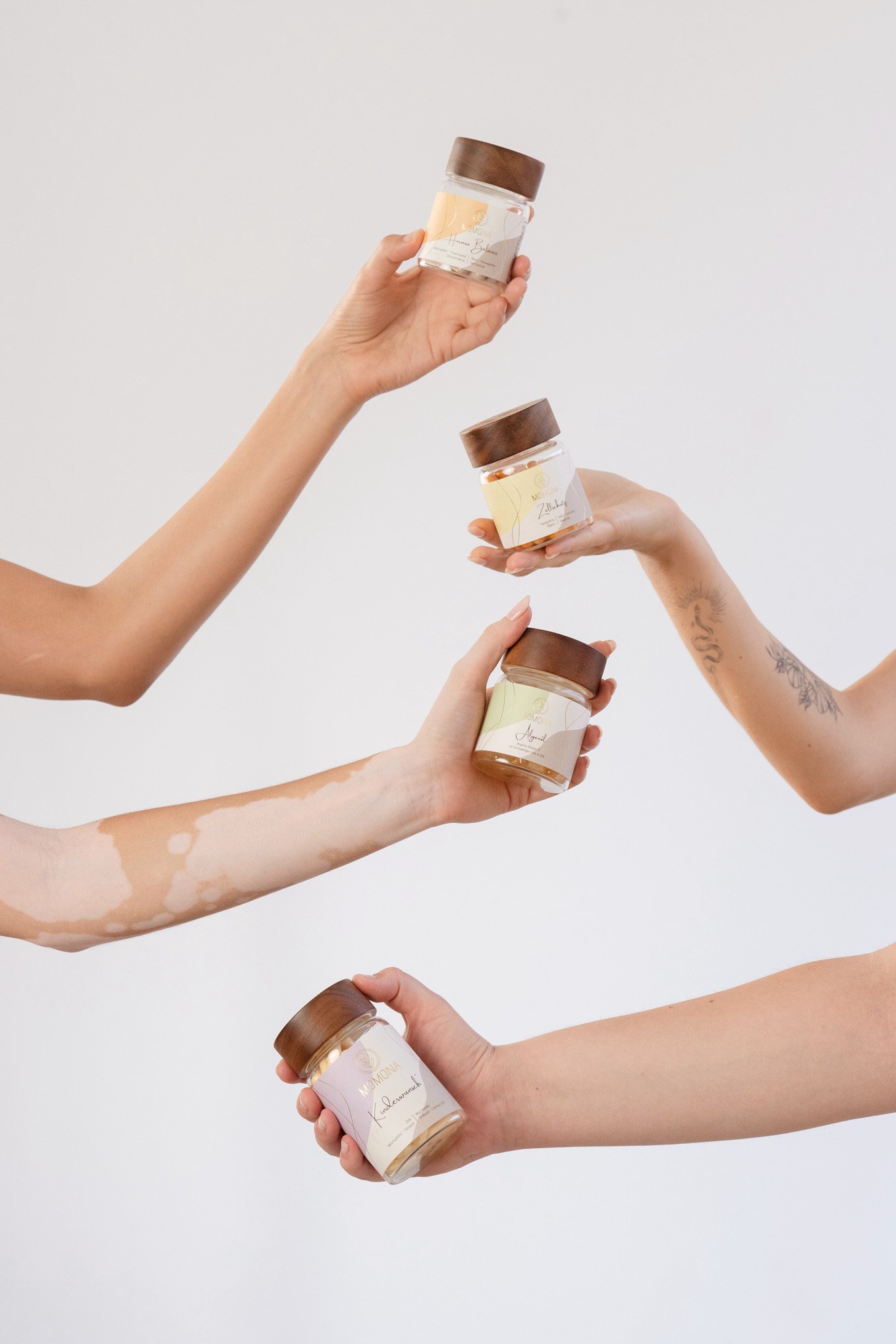 Four hands holding Momona supplements jars with brown lids against a plain background shot by Barcelona Product and Brand Photographer Julia Malinowska.