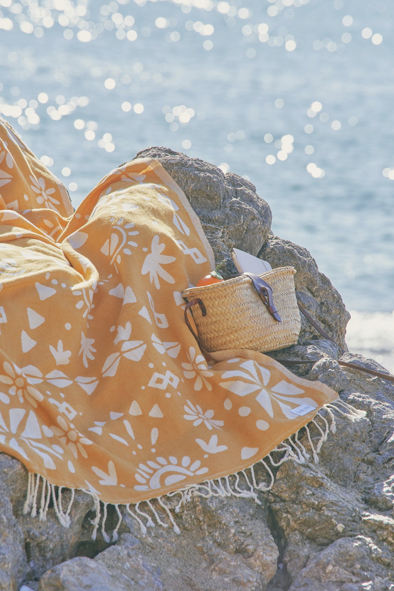 Orange blanket with white patterns on rocks near ocean