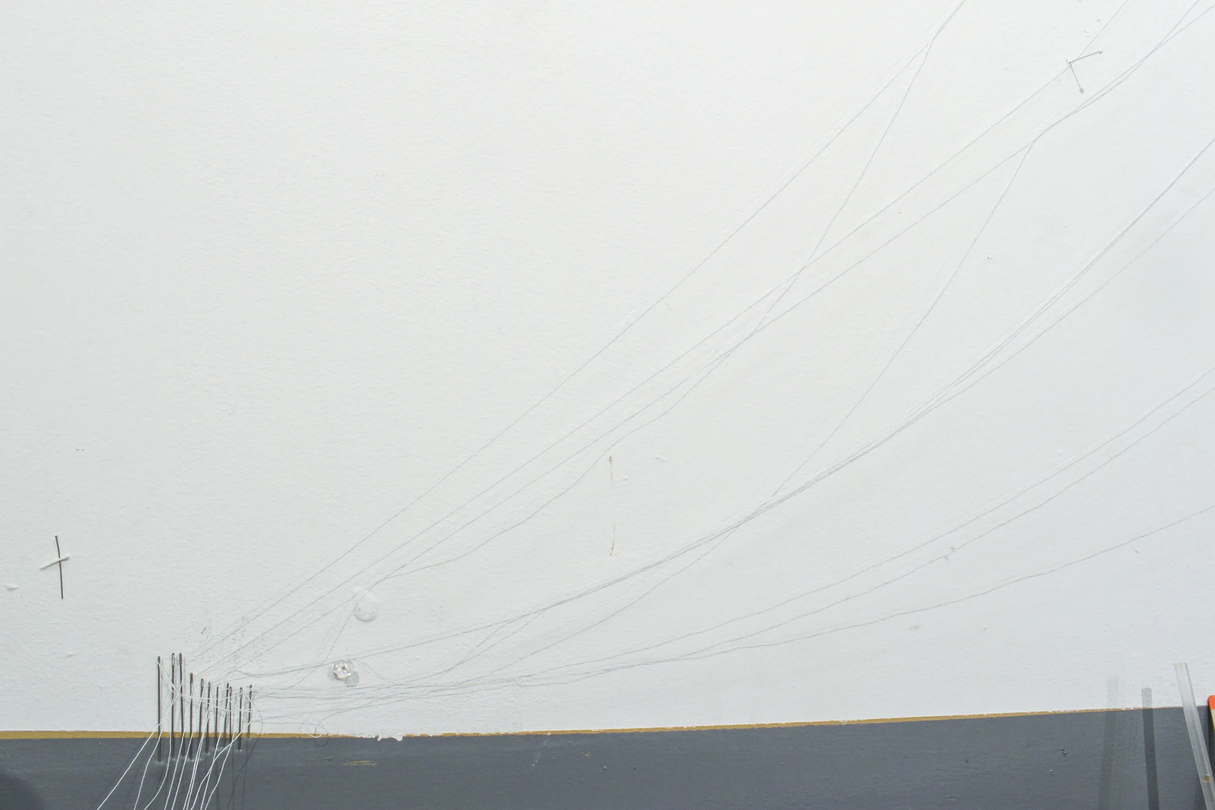 Detail. Pins, thread, plastic straw on wall.