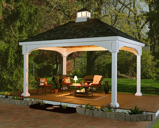 A white outdoor gazebo with seating, lamps, and decor in a backyard with trees.