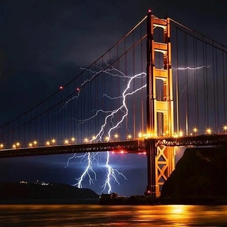 Lightning strikes near the Golden Gate Bridge at night, illuminating the dark sky and reflecting off the water below.