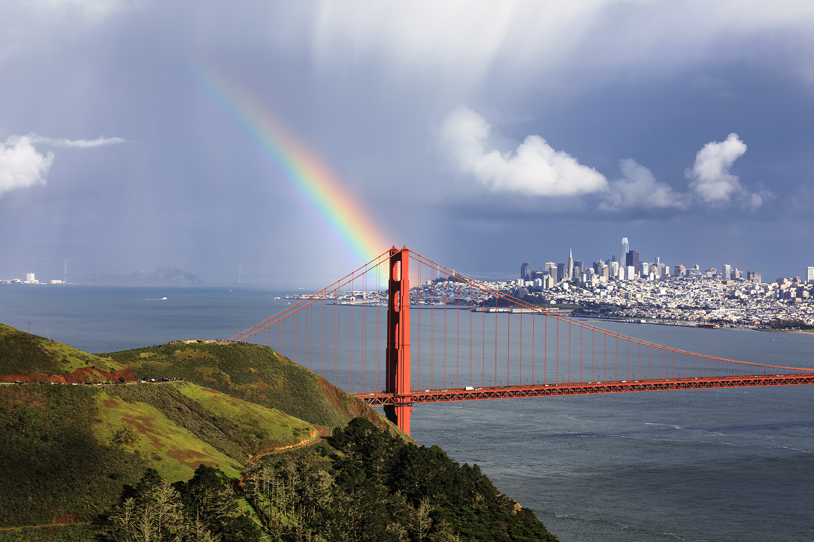 Golden Gate Bridge with a rainbow in the sky and San Francisco skyline in the background.