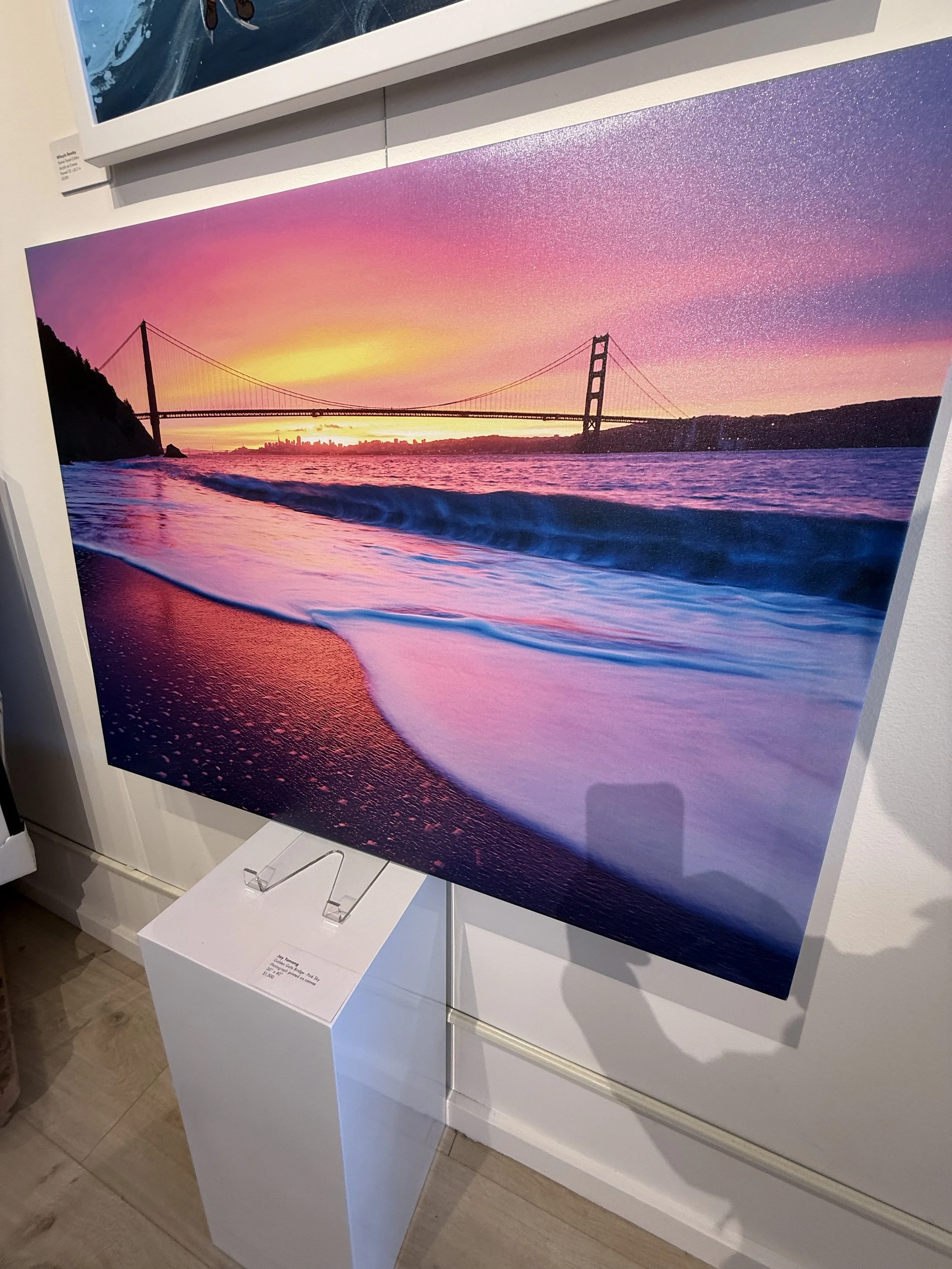 A vibrant photograph of the Golden Gate Bridge at sunset with colorful pink, purple, and yellow sky, captured from the water with waves in the foreground.