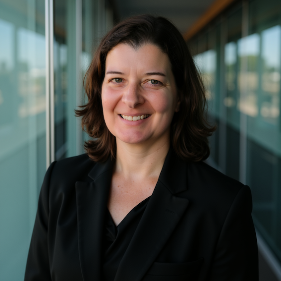 Professional woman with shoulder-length dark hair smiling in a business suit outdoors on a balcony or walkway