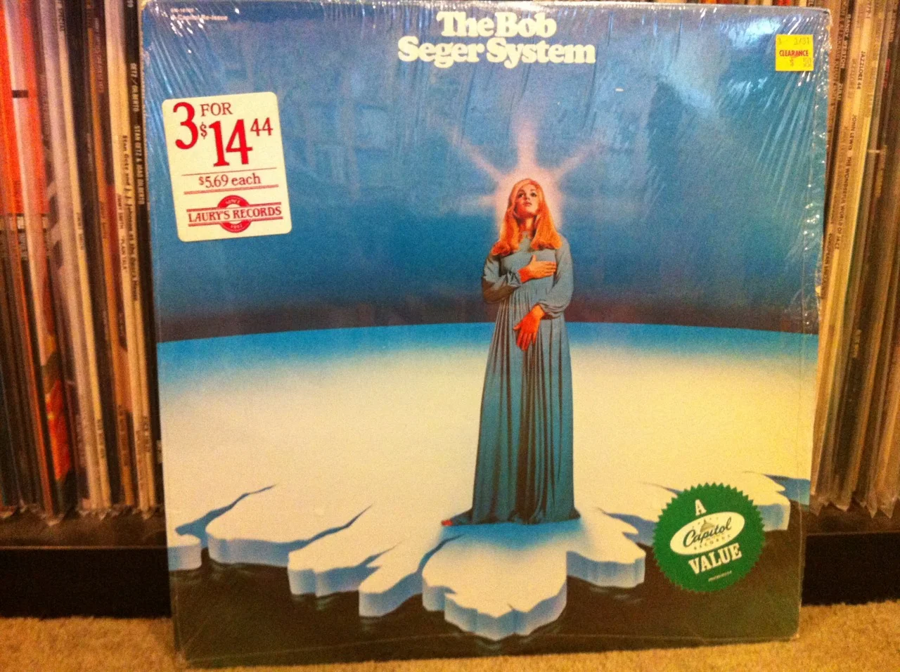 Bob Seger System Is No Silver Bullet!
No way. It’s a rock ‘n’ roll kick to the skull. Just the way I like it. Fact is, the first track – Ramblin’ Gamblin’ Man – kicks you in the head and then stomps your solar plexus after you fall to the ground shaking like your grandma’s bundt cake shaped lime jello.
I wanted to hate this slab of wax from 1968 – The Bob Seger System’s first LP – based on my experience with 1980s truck commercials drenched in MOR rock music from Bob Seger. Thing of it is, when you hear that much MOR rock music over and over all day long you begin to loathe it.
But there’s nothing to loathe in the grooves of Bob’s first outing as a rocker. The worst that can be said about this record is that some of the cuts are a bit hippy dippy (“Gone” comes to mind).
But when the Bob Seger System nails it – “Tales Of Lucy Blue”, “Down Home”, “Ivory”, “White Wall” and the title track – they really hammer it in. If Vice President Biden were to ask me to describe this album in terms he’d understand, I’d probably say it was musculoskeletal psychedelic rhythm ‘n’ blues with a dollop of country folk thrown in to scare the crap out of you.
And, that’s what this record did for me. It scared the crap out of me. Because there’s a lot to love about it. And I wasn’t ready to love Seger. There’s thudding, pounding, hammering, screeching and a few moments where you stick your head out the window to escape the smoke and breathe in some of that sweet, cool Motor City air. I love those things in a rock record. A rock record that sounds like Detroit in 1968.
I can actually imagine UAW workers listening to this record as they pounded together a car with some serious curb weight. Sensational. And that my friend, is factual.
Listen to Ramblin’ Gamblin’ Man by clicking this very link!
For weirdos only: Allow me to get on a teensy weensy soap box for a second. A close look at this record would lead the uninitiated to think I dropped $5.69 for this LP at Laury’s Records. A great deal by me. A real close look will reveal a “Clearance $.50” sticker top right. That’s right, weirdos. Yours truly scored this slab of wax a mere two weeks ago at a used book store for half a buck. Shrink wrap intact. Sure, it’s an early 80s reissue. But 50 cents? Mint condition. It boggles the mind. Talk about an inflation beater! That’s twelve full inches of artwork (Kinda naughty in this case if you look close. Shame on you Capitol Records!) with eleven songs carved neatly into two sides of a vinyl story created by someone desperately trying to tell you something they think is important. Try finding a music file at a used bookstore that can duplicate this action. Go ahead, try it. Take that, digital!