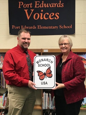 Mrs. McGrath presents Mr. Cronan a sign to be hung on the Elementary School celebrating the achievements of the school in helping to protect the Monarch Butterfly. Photo via Port Edwards School District .