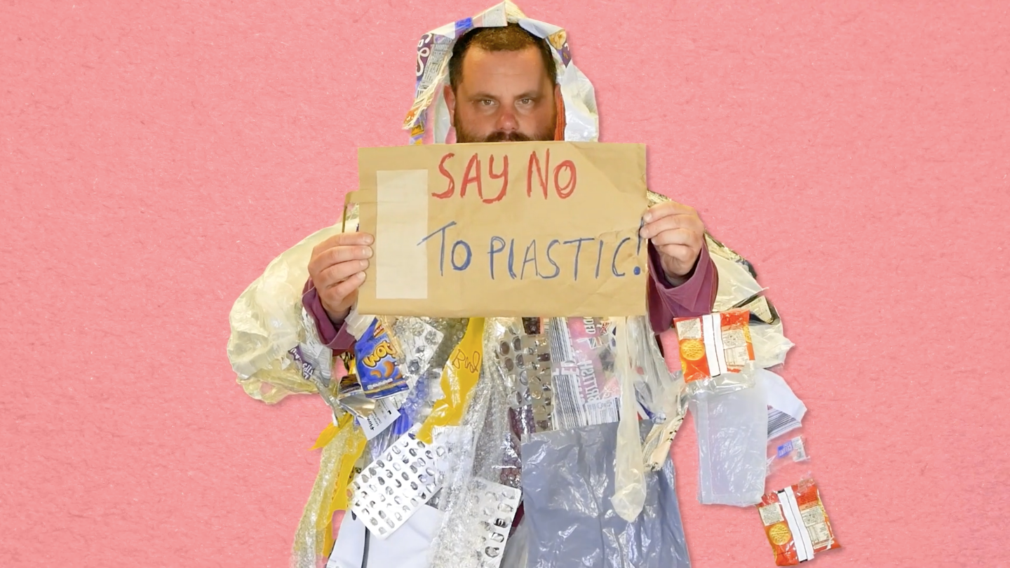 A man wearing plastic rubbish as clothing carrying a placard reading 'SAY NO TO PLASTIC'