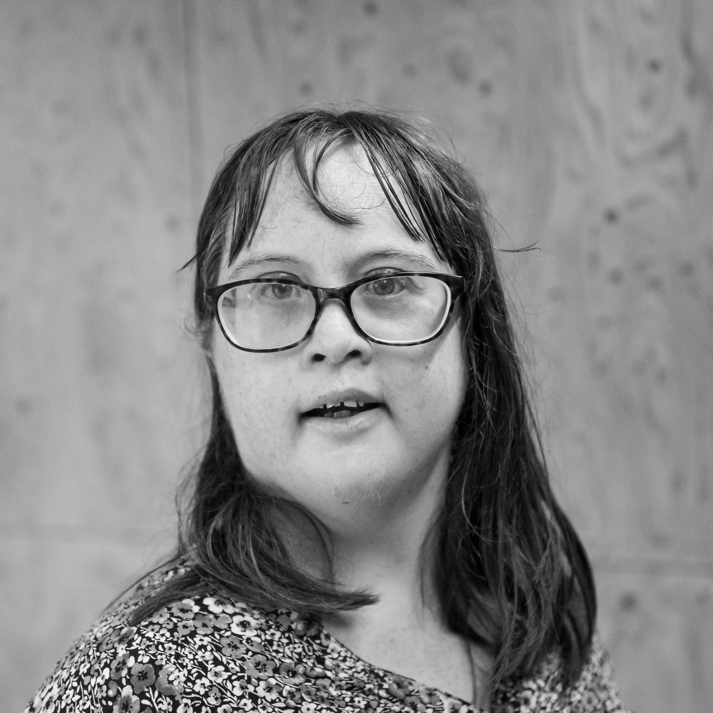 head and shoulders image of a woman with shoulder length brown hair wearing glasses and a patterned v neck top