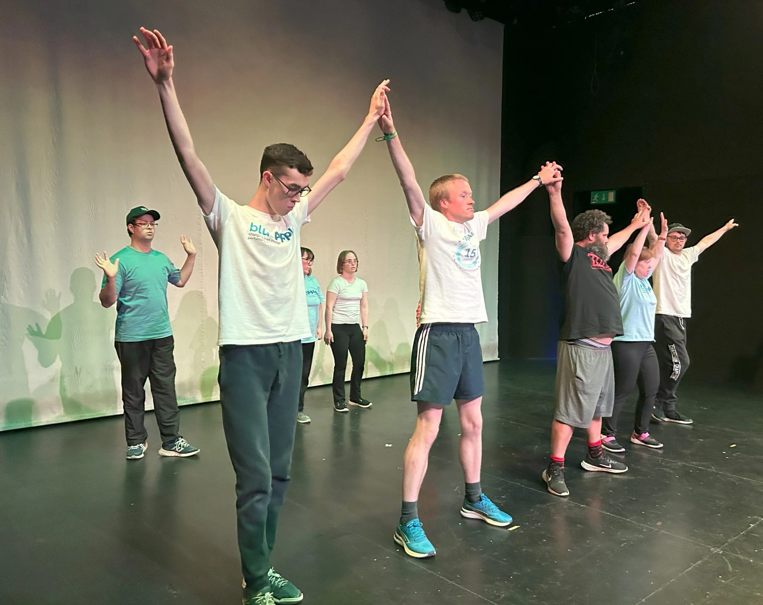 A group of dancers in a studio hold their arms up joined together
