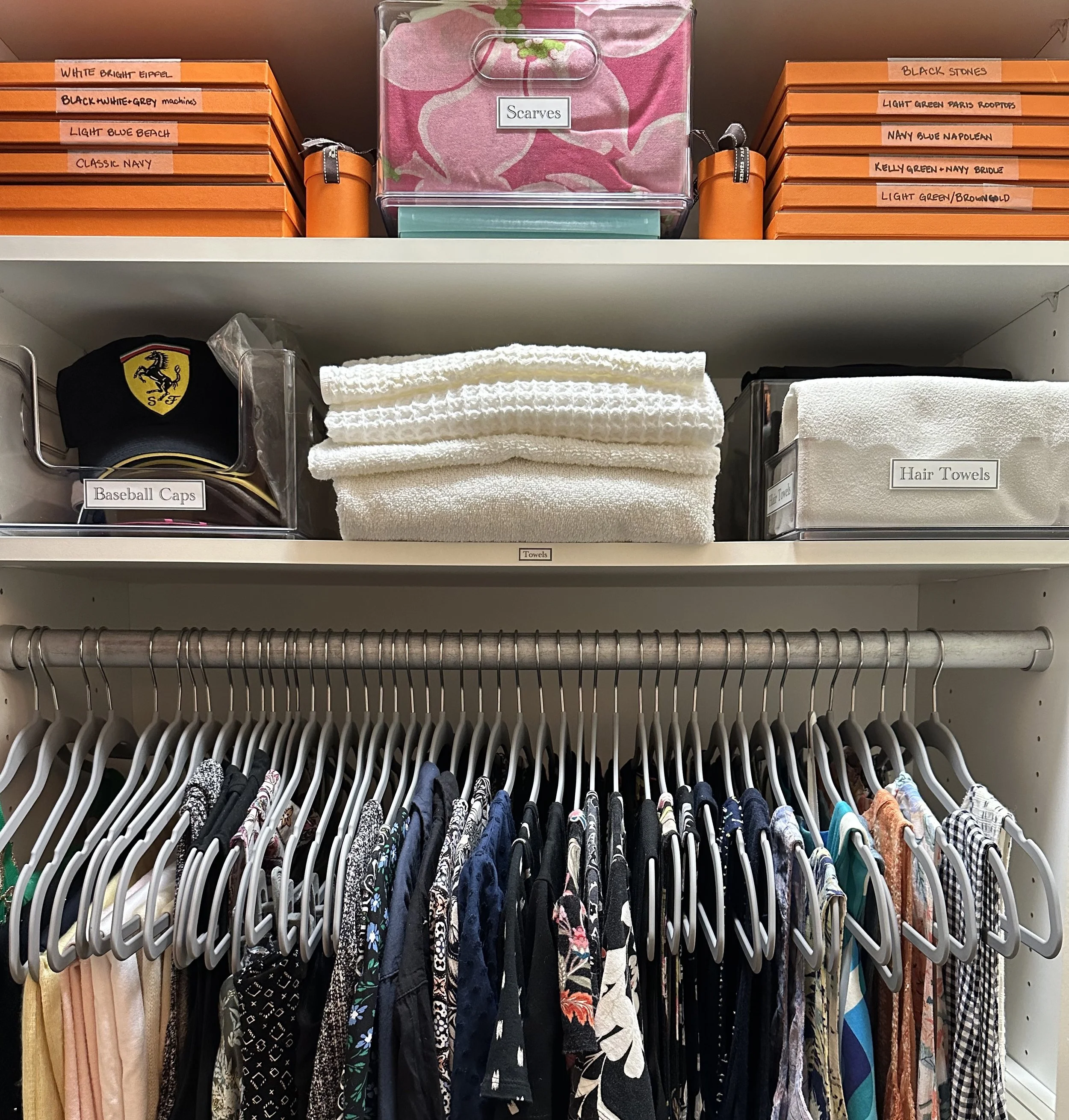 Closet with clothing hanging on rubberized gray hangers, folded towels, scarf collection, baseball hats