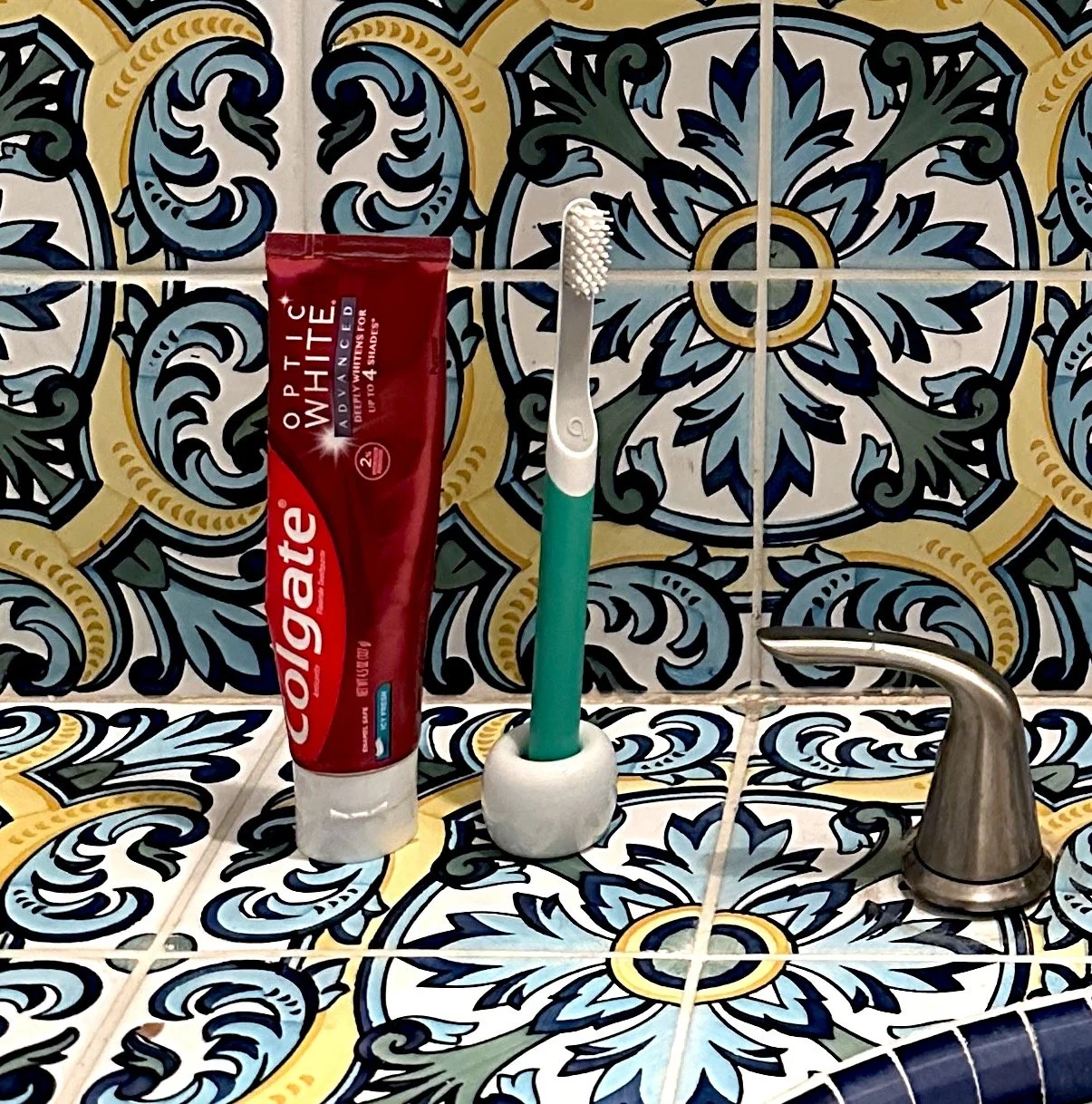 Floral blue green yellow white bathroom tile, quip toothbrush, Colgate toothpaste