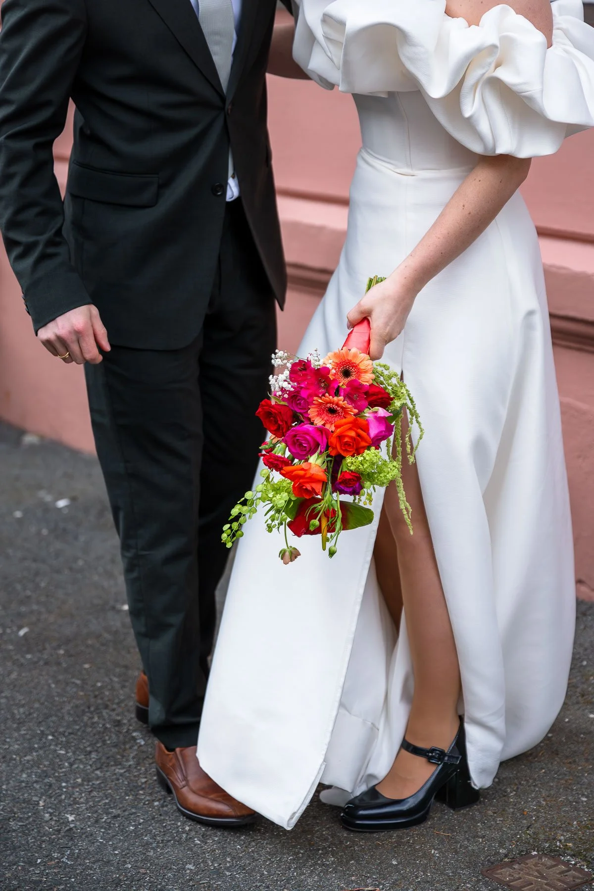 Hvit brudekjole og sort dresset bryllupsgjest med fargerik brudebukett.