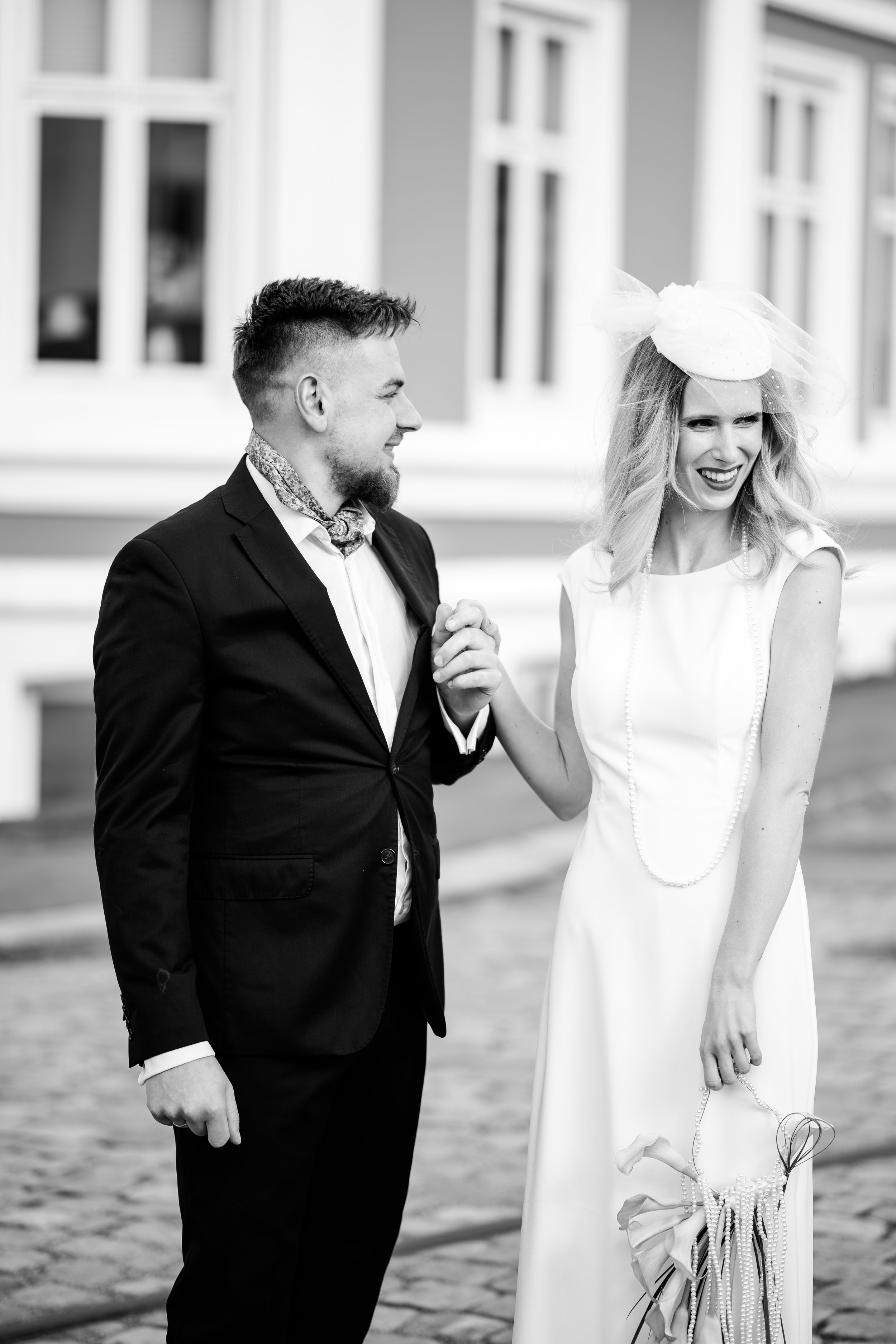 Et svart-hvitt bilde av en smilende kvinne i brudekjole og en mann i dress som holder hverandres hender.